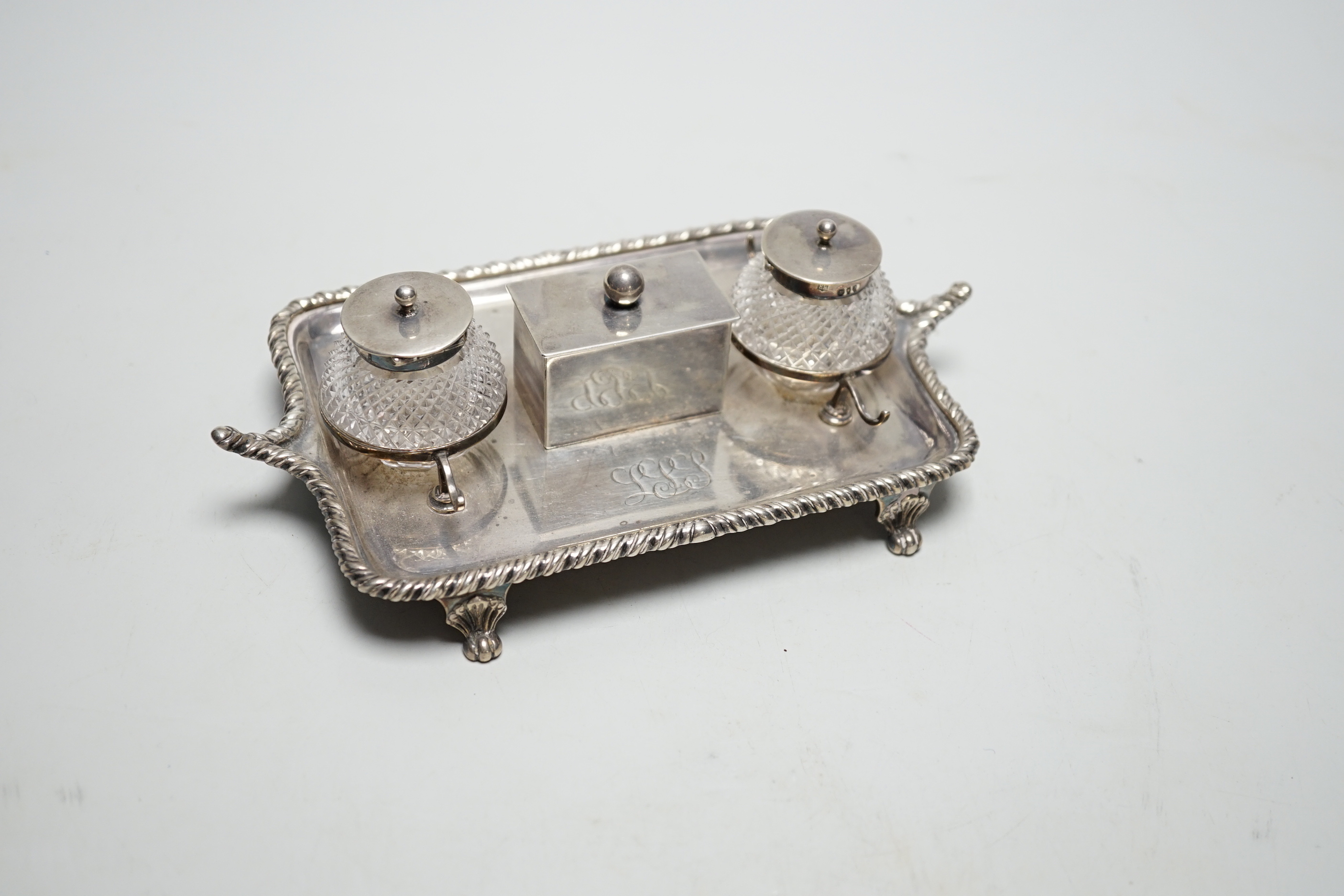 A late Victorian silver rectangular inkstand, with two mounted cut glass wells, central lidded compartment and two pen rests, Edward Hutton, London, 1890, 19cm, weighable silver 9oz.